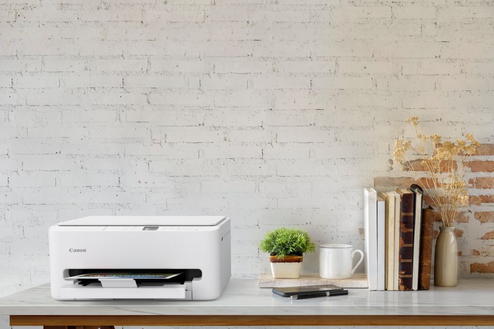 Product shot of a Canon all-in-one inkjet printer on an office desk with a printed colour document.